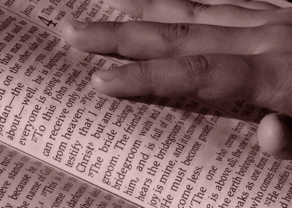 photo of hand resting upon opened Bible