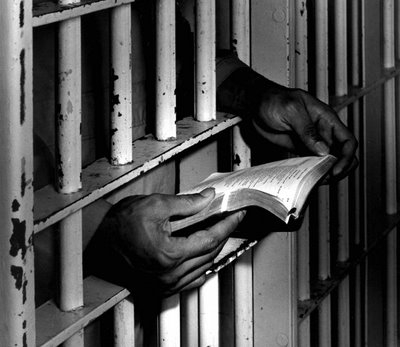 photo of inmate's hands reaching out of prison bars and holding Bible